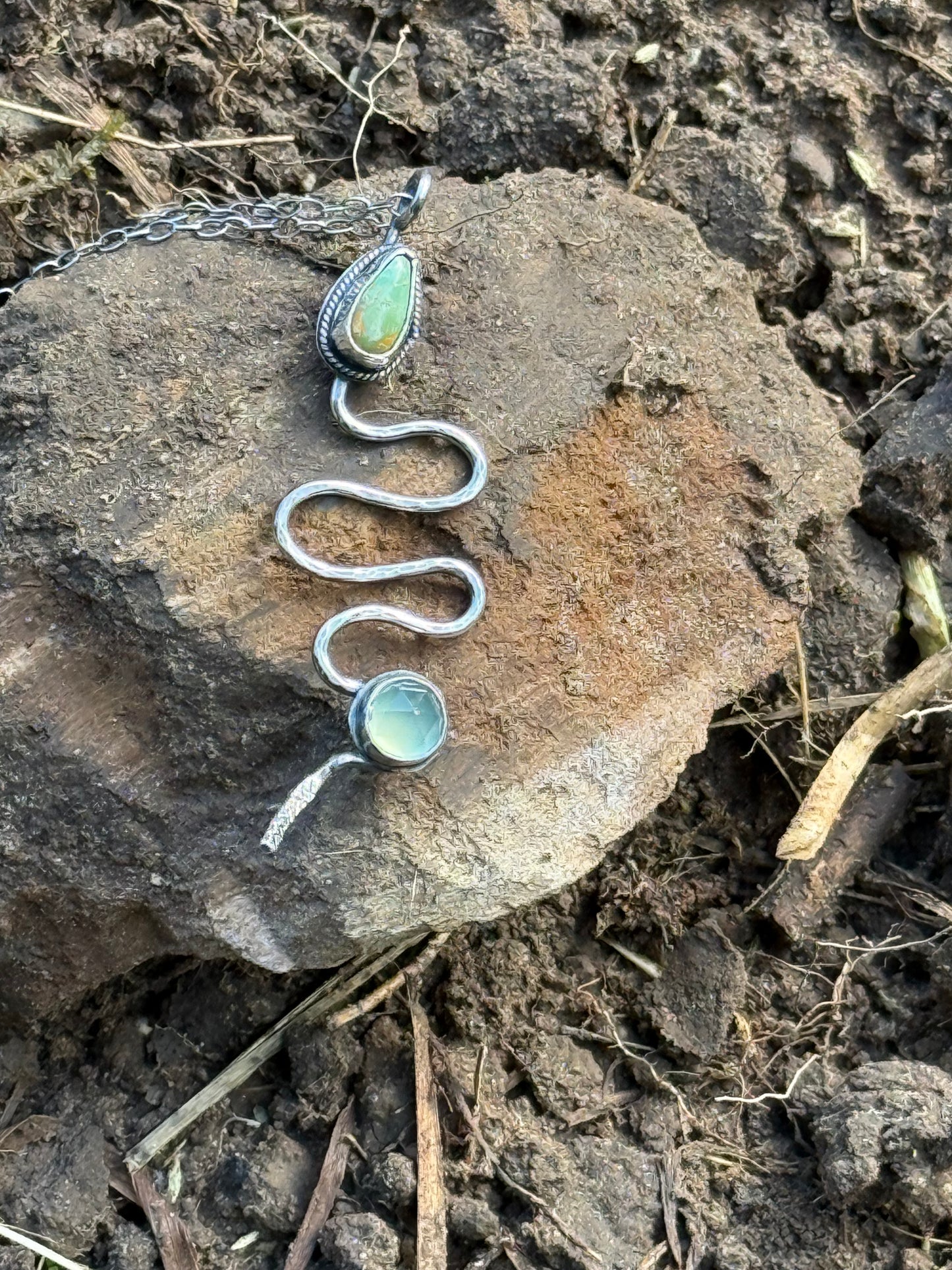 Silver snake-shaped necklace with turquoise stones on a rock