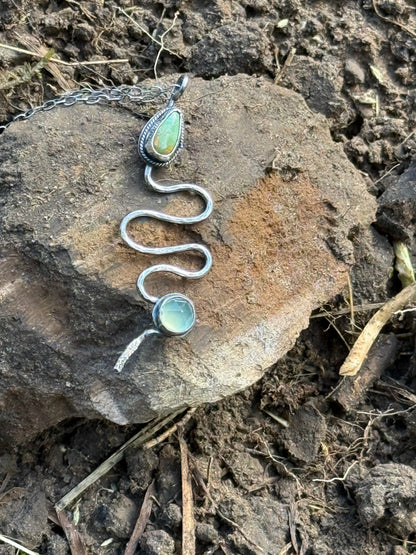 Silver snake-shaped necklace with turquoise stones on a rock