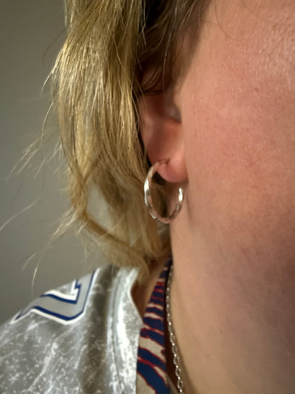 Close-up of a person wearing a gold hoop earring with a blurred background