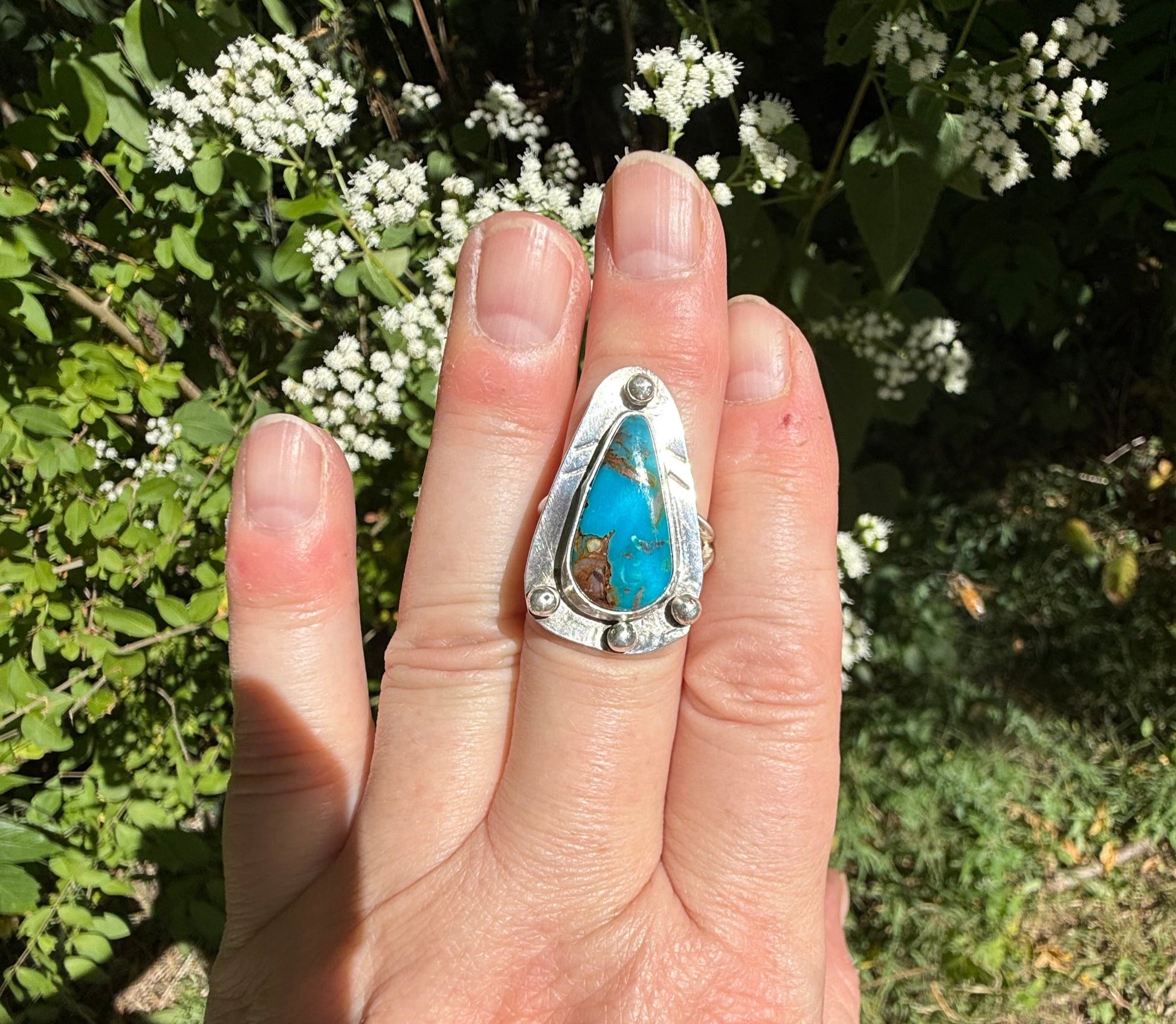 Hand wearing a silver ring with turquoise stone against a natural background