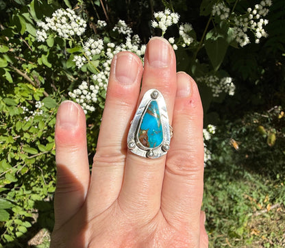 Hand wearing a silver ring with turquoise stone against a natural background