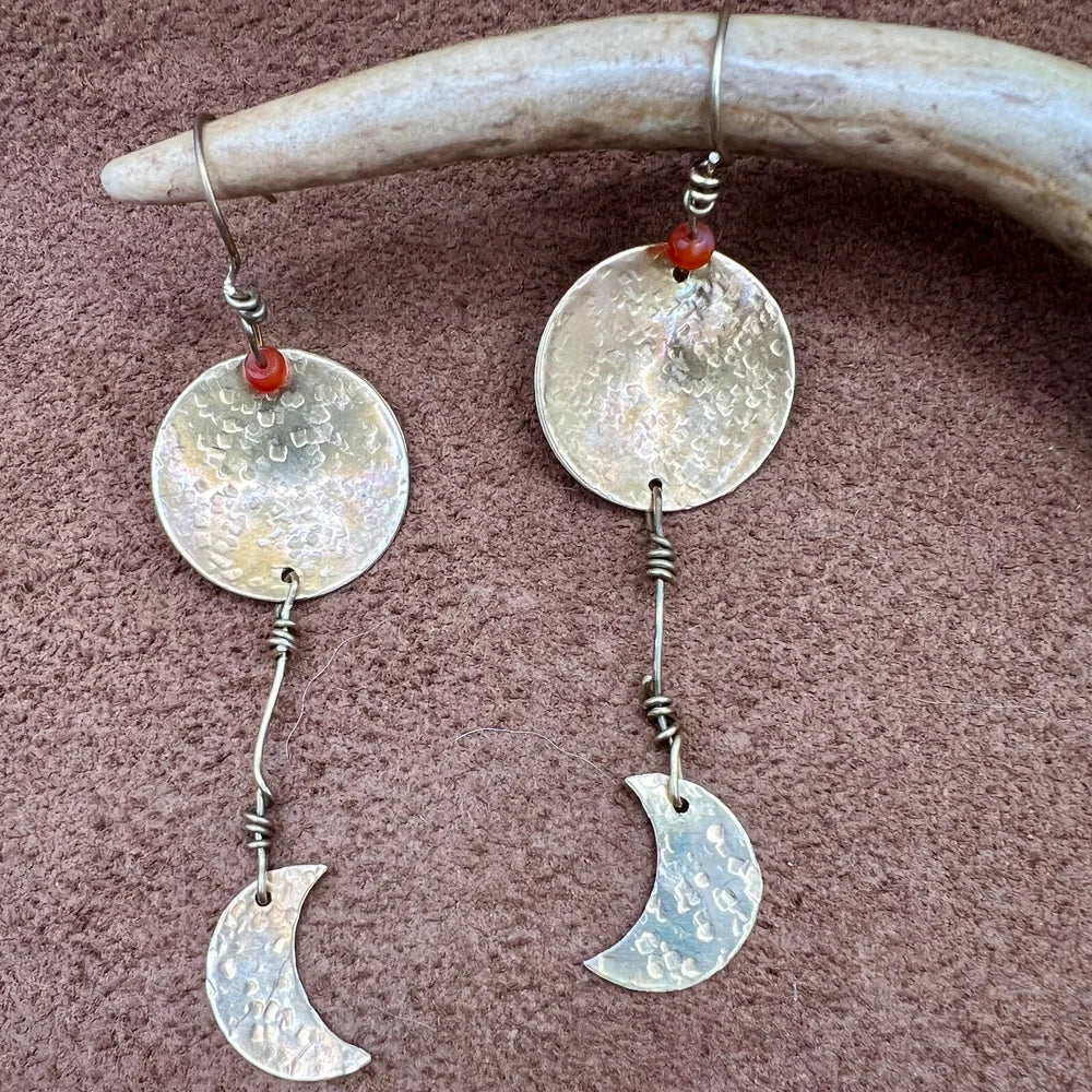 Silver earrings with circular and crescent moon designs hanging from a antler.