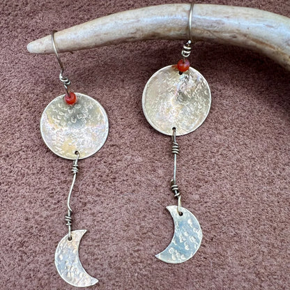 Silver earrings with circular and crescent moon designs hanging from a antler.